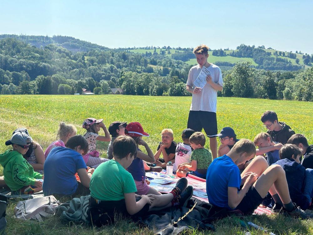 Skupina dětí s vedoucím na louce v přírodě